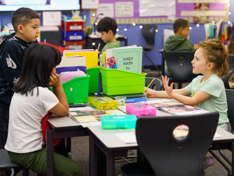 Three students sit at tables with files of instructional materials.