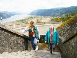 Two women ascend outdoor stairs at Vista House with the Columbia River Gorge in the background.