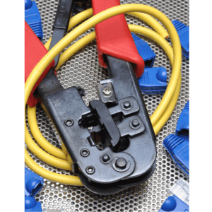 A photo of a cable crimping tool, wrapped with yellow network cables, lies on a corrugated metal surface flanked by a scattering of blue cable caps